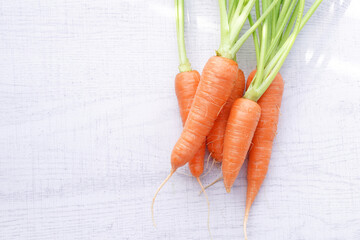 Organic mini carrots with leaves isolated on white wood background.
