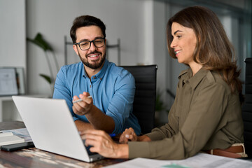 Obraz na płótnie Canvas Two happy busy business people entrepreneurs team checking data using laptop at work in office. Mature executive manager talking to colleague explaining online results having discussion at meeting.