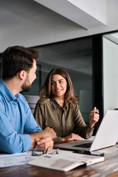 Smiling professional business people using laptop having conversation working in office discussing corporate strategy at workplace. Two happy colleagues man and woman talking at work. Vertical photo