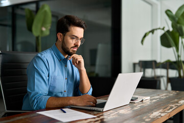 Serious businessman looking at computer thinking on online investment or software development using...