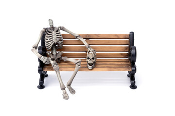 Haunted by ghosts. Human headless skeleton sits near his skull with a ghostly face on old wooden bench isolated on white background.