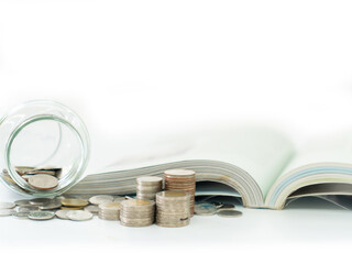 A coin jar and an open book are placed beside a pile of coins.