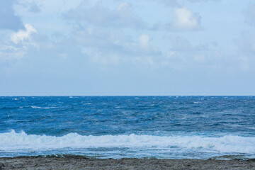 Obraz premium Rough Ocean Waves Impacting a Rocky Beach: A powerful scene of wind-driven ocean waves crashing and creating sea spray as they hit a dark, rocky shore.