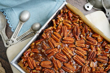Decadent Pecan Brownies with caramel in a baking pan with light blue napkins.  Freshly baked brownies in a pan with measuring spoons and napkins on a wood counter top.
