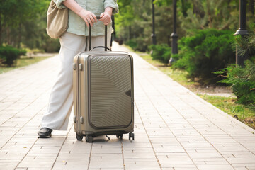 50s year woman with suitcase and bag stay on green summer alley, vacation, travel, outdoor scene