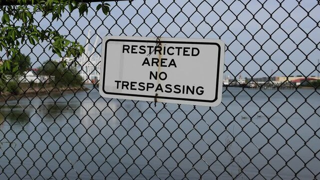 restricted area no trespassing sign on black metal chain link fence in front of shipping docks in bayonne new jersey (infrastructure industrial ship container delivery security international tariff)