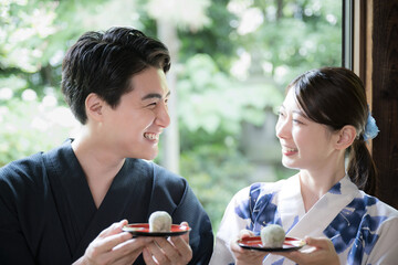 縁側でおまんじゅうや和菓子食べる浴衣の男女　旅館や宿の旅行イメージ