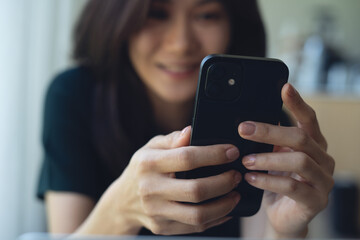 Closeup, happy asian woman using mobile phone for online meeting during working on laptop computer at coffee shop. Young casual business woman working remotely and using smartphone for video call