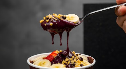 Close-up of an açaí spoonful with dripping textures and highlighted toppings, set against a dark background for visual focus and striking shadow contrast