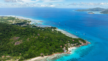 Island with lush green hills and turquoise ocean waters, viewed from above. La Digue, Seychelles.