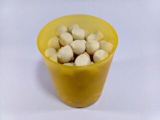 A translucent yellow plastic cup filled with numerous small, pale, round fish mackerel crackers, a...