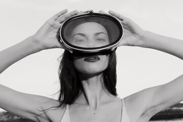 Woman holding a retro glass headset against a cloudy sky background, showcasing a fusion of past...