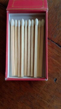 Close-up of a red matchbox filled with wooden matches with white tips, arranged neatly inside on a wooden table background