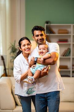 Young Indian parents standing with baby boy in arms inside modern stylish living room at home