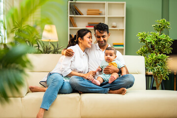 Obraz premium Young Indian couple sitting with baby boy indoors showing care, happiness, modern family lifestyle
