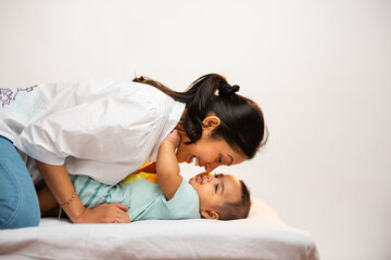 Smiling Indian parents interact joyfully with newborn baby boy lying on soft white bed