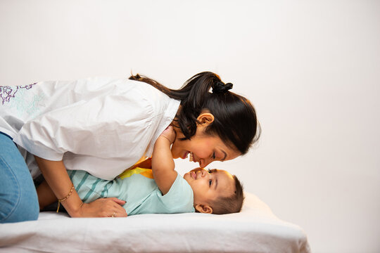 Smiling Indian parents interact joyfully with newborn baby boy lying on soft white bed