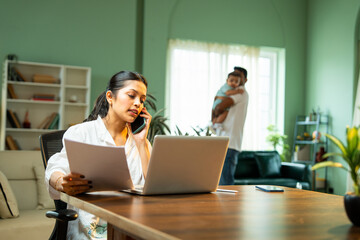 Plakat Mother working from home using laptop celebrates project success while father holding baby