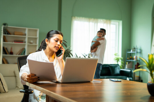 Fototapeta Mother working from home using laptop celebrates project success while father holding baby