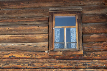 An old wooden log house built in the 19th century. Windows in a rustic house with fabric curtains . Life in the countryside. The history and traditions of rural life.