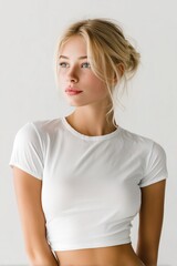 Fototapeta premium A young woman with blonde hair styled in a loose bun, wearing a fitted white t-shirt mockup. She has a natural, soft expression and is posed against a light, neutral background.