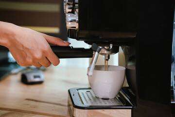 Barista grinding coffee beans and pouring espresso from machine in café, showing close-up of professional preparation of hot aromatic drink.