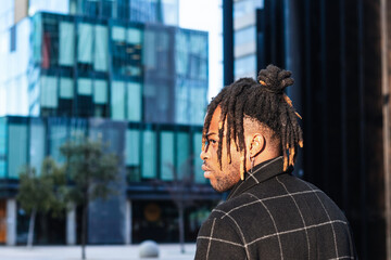 Side view African American man with dreadlocks in buns on blurred cityscape looking away