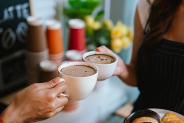 Two friends clink coffee mugs in a cozy café, enjoying a warm beverage together, symbolizing friendship, relaxation, and shared moments.