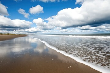 Coastal scenery of sandy beach and blue sky reflected in ocean water