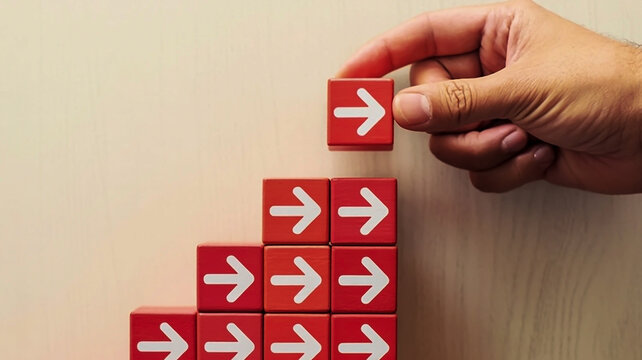A minimalist business growth concept image shows red matte cubic blocks in ascending steps with white heart icons, a hand placing the top block, and a black curved arrow