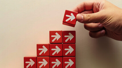 A minimalist business growth concept image shows red matte cubic blocks in ascending steps with white heart icons, a hand placing the top block, and a black curved arrow
