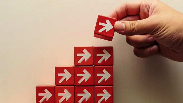 A minimalist business growth concept image shows red matte cubic blocks in ascending steps with white heart icons, a hand placing the top block, and a black curved arrow