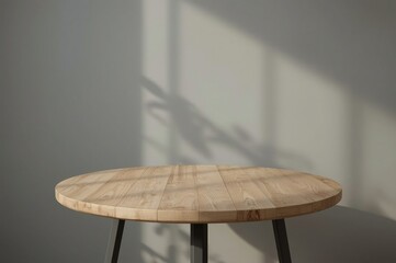 Empty round wooden table with black legs against a neutral wall with sunlight shadows