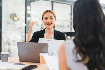 Young businesswoman presenting financial report with laptop and coffee cup in modern office, showing confident and positive expression during meeting