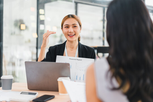 Young businesswoman presenting financial report with laptop and coffee cup in modern office, showing confident and positive expression during meeting - Powered by Adobe