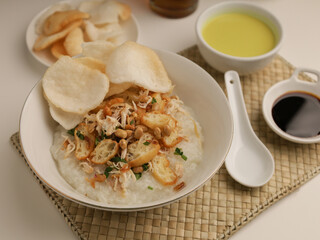 Rice porridge in a bowl, served with shredded chicken, chicken stock, fried shallot and crackers
