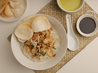 Rice porridge in a bowl, served with shredded chicken, chicken stock, fried shallot and crackers