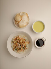 Rice porridge in a bowl, served with shredded chicken, chicken stock, fried shallot and crackers