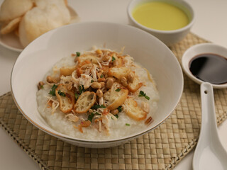 Rice porridge in a bowl, served with shredded chicken, chicken stock, fried shallot and crackers