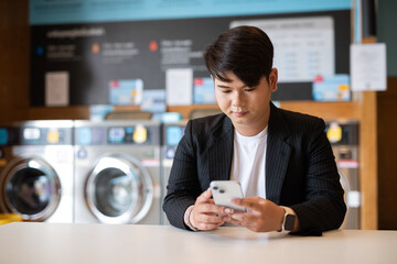Young gay man in laundry shop using mobile phone