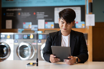 Gay businessman working on tablet computer in laundry shop