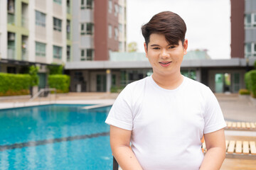 Happy young gay man sitting next to swimming pool during summer