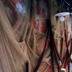 Fishing nets hanging on a worn red wall with peeling paint and a vintage lamp. Rustic marine scene with strong texture, perfect for nautical, vintage or conceptual backgrounds.