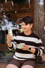 Portrait of a young gay man sitting outside of cafe restaurant during summer