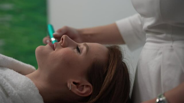 Cropped shot of professional beautician performing microneedling treatment with dermapen on female patient forehead, targeting skin rejuvenation enhancing collagen production, close-up, slow motion