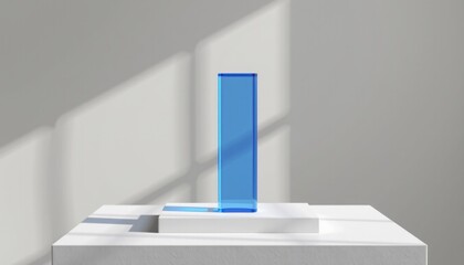 A minimalist blue glass rectangle stands upright on a white geometric base, with soft shadows and natural light on a gray wall.