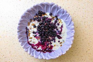 Blueberry granola with yogurt in purple bowl on speckled countertop