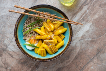 Turquoise bowl with korean traditional snack meal rabokki on a brown granite background, horizontal shot, above view