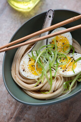 Udon noodles with boiled chicken egg and spring onion in a green bowl, vertical shot on a brown granite surface, middle close-up