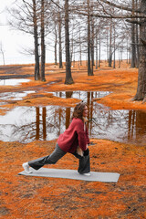 Young woman performs lunging exercise on mat surrounded by vibrant autumn forest scenery near a...